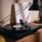 Salon 1 Audio Ortofon 2M Black moving magnet cartridge installed on a black turntable in a warm, dimly lit room.