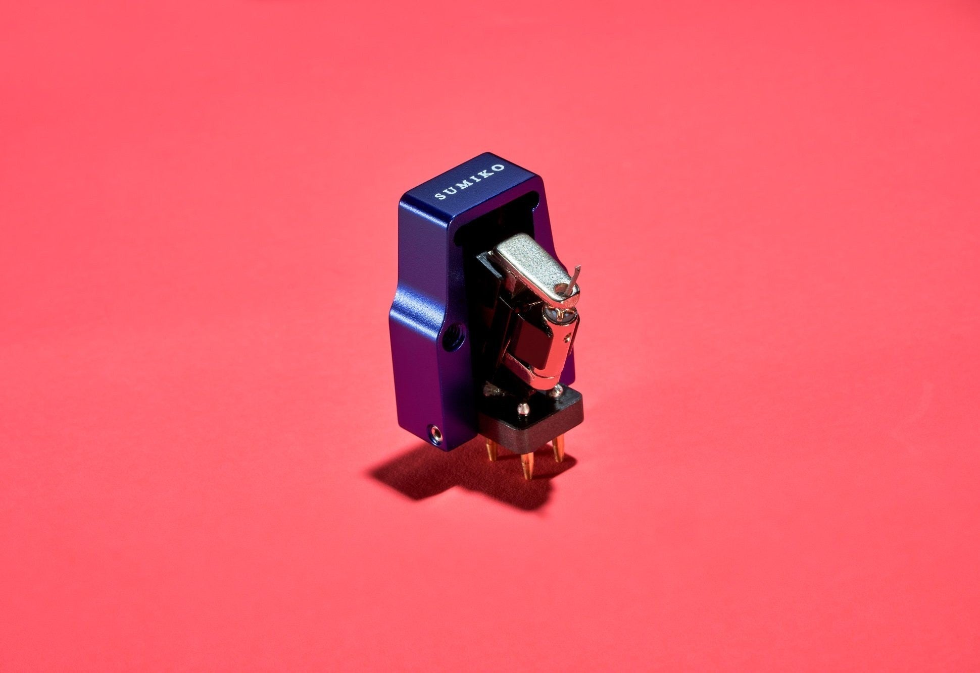 Salon 1 Audio Sumiko Songbird Low moving coil cartridge in blue with an open-body design on a vibrant red background.